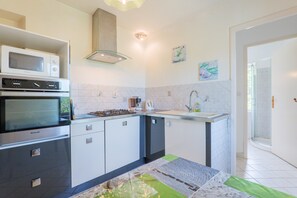 Una cocina moderna con microondas, horno y cocina a gas, un lavamanos y una cabina de ducha con mampara de cristal.