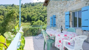 A stone building with a balcony, outdoor seating, and a view of a forested hillside. - La Cupinoise Gite in Ardèche Nature, Terrace & Valley View (Antraigues sur Volane)