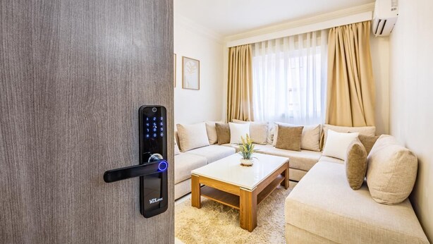 A modern living room with a sofa, a coffee table, and a door with a digital lock. - Luxury Apartment in Marrakech (Marrakech)