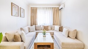 A living room with a beige sectional sofa, a white coffee table, and a large window with sheer curtains. - Luxury Apartment in Marrakech (Marrakech)