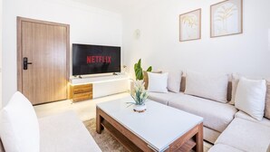 A modern living room with a flat-screen TV, a sofa, a coffee table, and framed artwork on the wall. - Luxury Apartment in Marrakech (Marrakech)