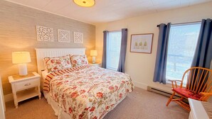Une chambre à coucher avec un lit, des tables de chevet, une chaise et une fenêtre avec des rideaux.