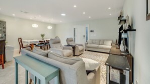 Uma sala de estar moderna com um sofá, poltronas, uma mesa de jantar e uma pequena escrivaninha.