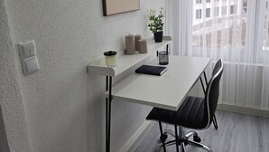 A modern room with a white desk, black chairs, a potted plant, and a large window with curtains. - Lovely home for you 2 (Biberach an der Riß)