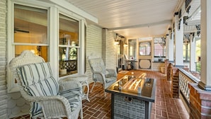 A covered porch with wicker furniture, a glass-top table, and brick flooring. - Pool | Hot Tub | 3 Min to Lake | Pets Allowed (Auburn)