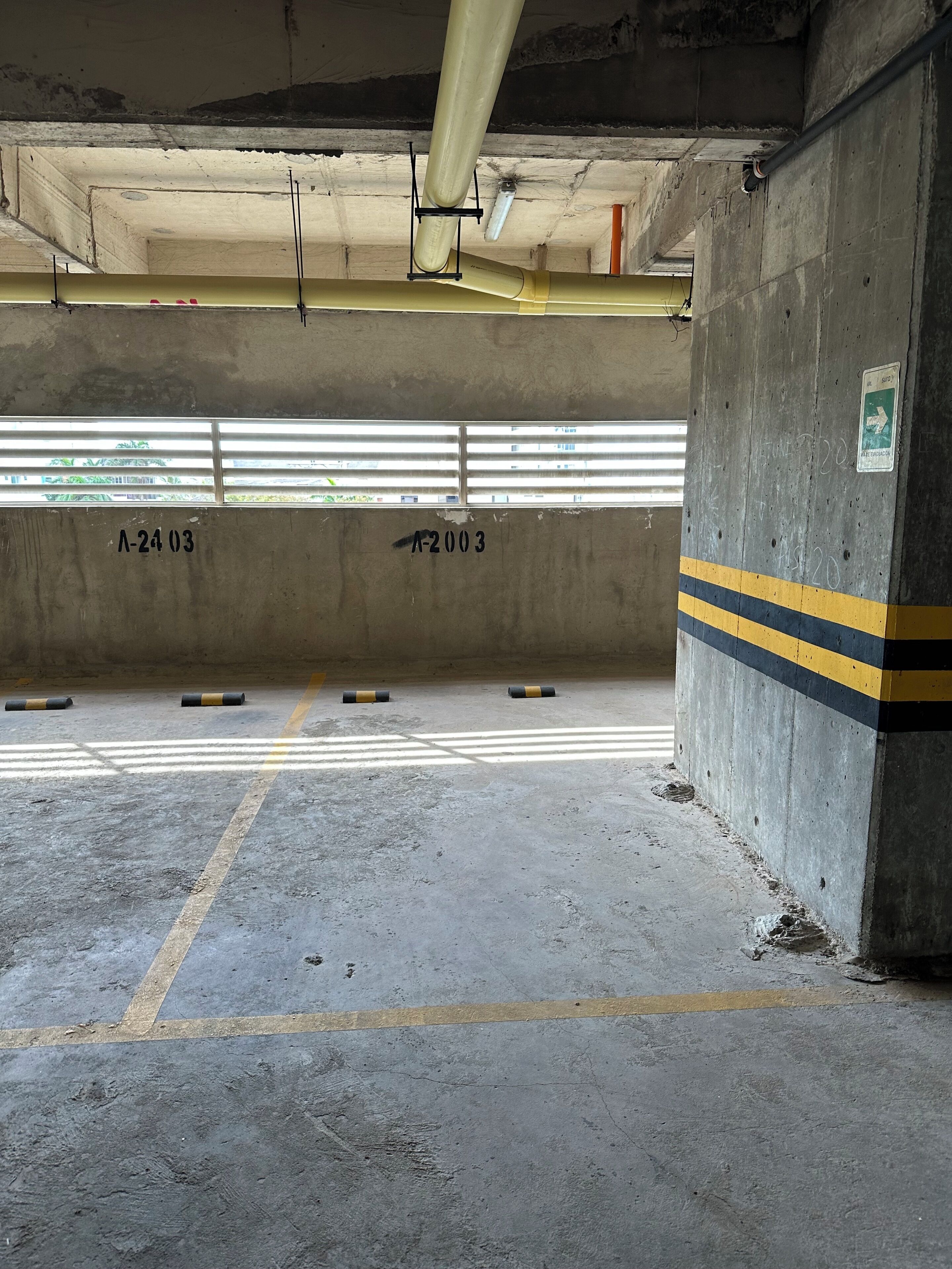 Un aparcamiento subterráneo con paredes de hormigón, líneas amarillas y negras a rayas, y espacios de estacionamiento numerados.