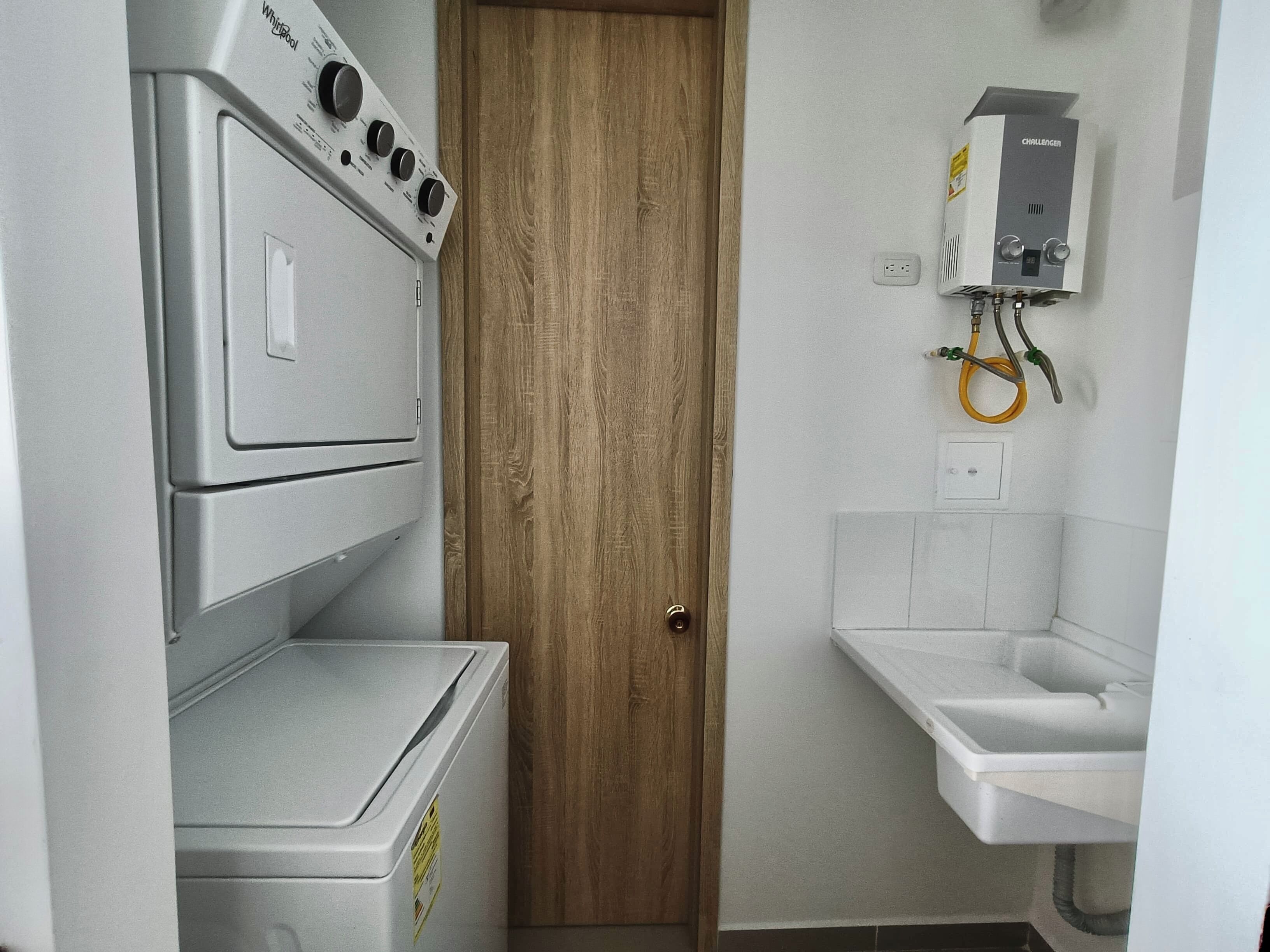 Un lavadero con lavadoras y secadoras apiladas, una puerta de madera y un lavabo blanco con manguera.