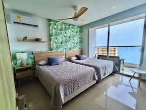 A modern bedroom with two beds, a ceiling fan, a large window with a view of a building, and a balcony with a chair. - Great sea views, near beach & historic center (Cartagena de indias)
