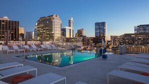 En pool på taket med solstolar och en stadsbild som bakgrund.
