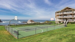 A beachfront property with a basketball court, a large building with multiple balconies, and a view of the ocean.