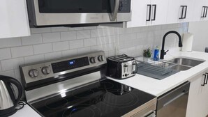 A modern kitchen with stainless steel appliances, including a microwave, oven, and stove. There is a toaster on the counter, and a sink with a faucet. - Mayfair Suite (Airdrie)