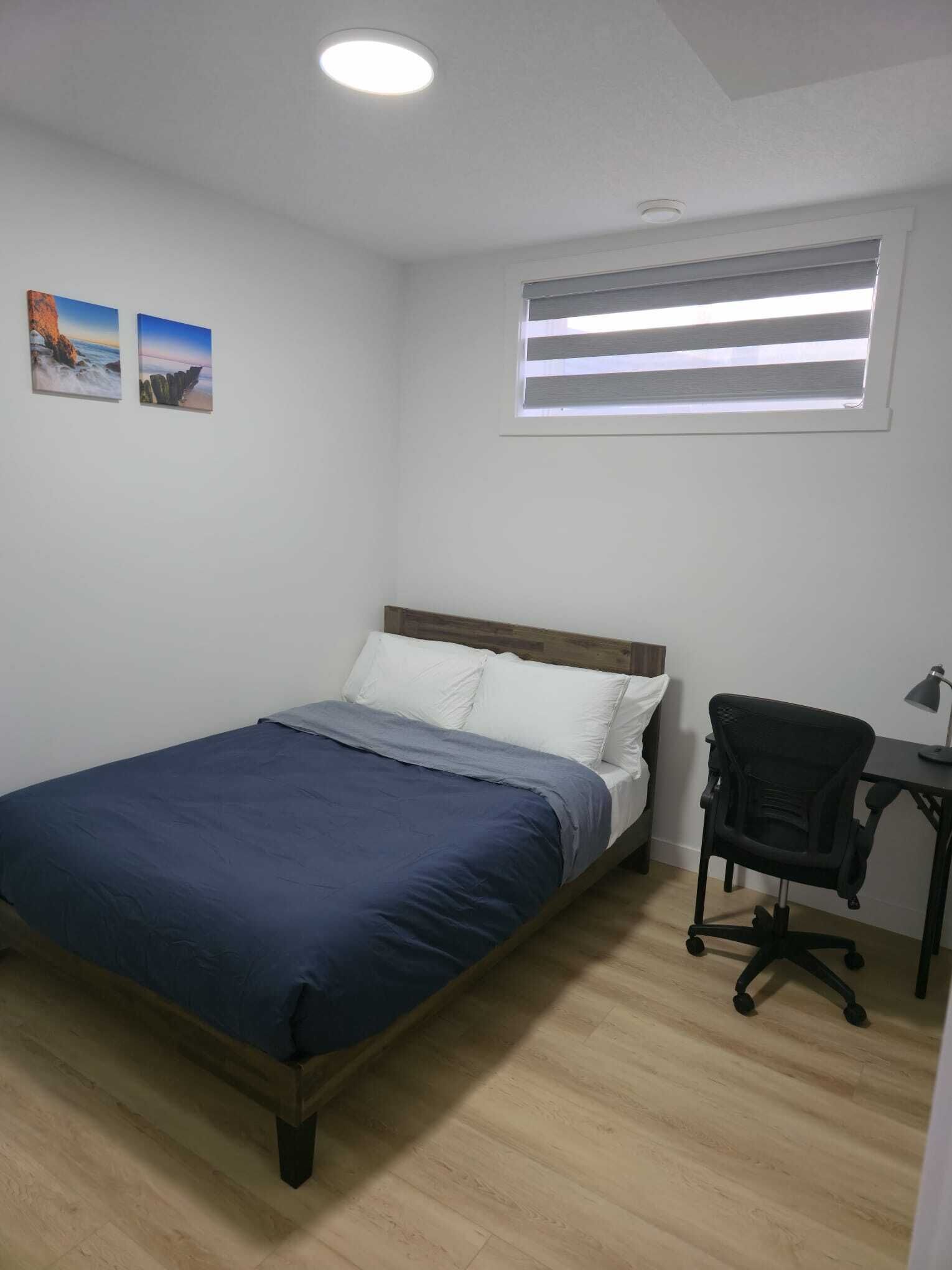 A bedroom with a bed, a desk, a chair, and a window with blinds.