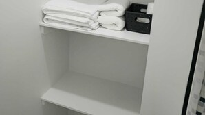 A white bathroom with a shelf holding folded towels and a black tray. - Mayfair Suite (Airdrie)