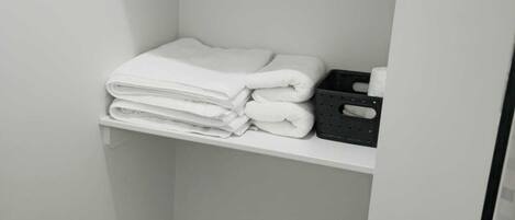 Une salle de bain blanche avec une étagère où sont pliées des serviettes et un plateau noir.
