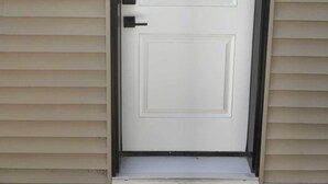 A white door with a black frame, a mailbox, and a small step leading to the door. - Mayfair Suite (Airdrie)
