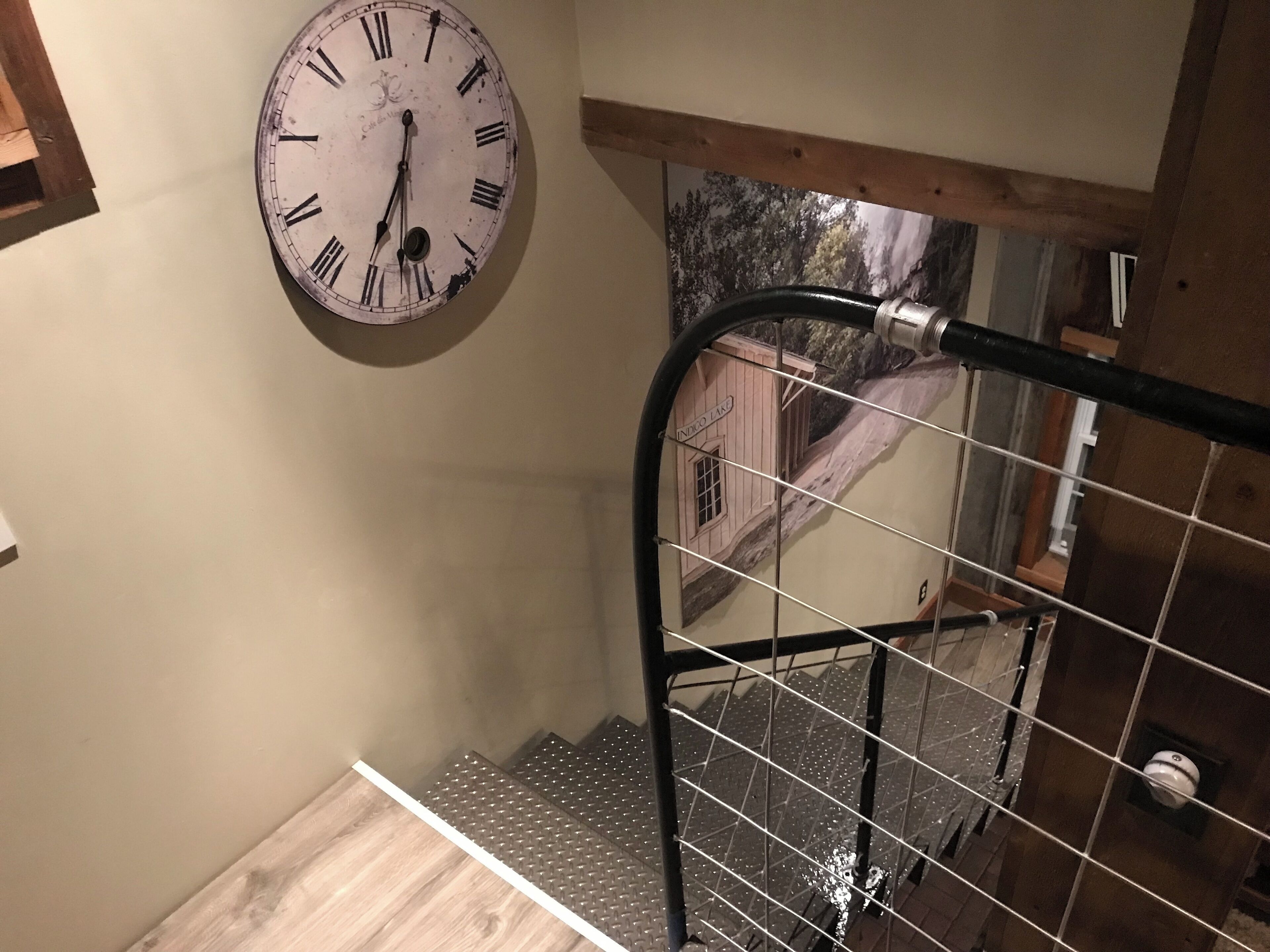 A staircase with a metal railing, a wall clock, and a window with a view of a building labeled "INDIGO LAND".
