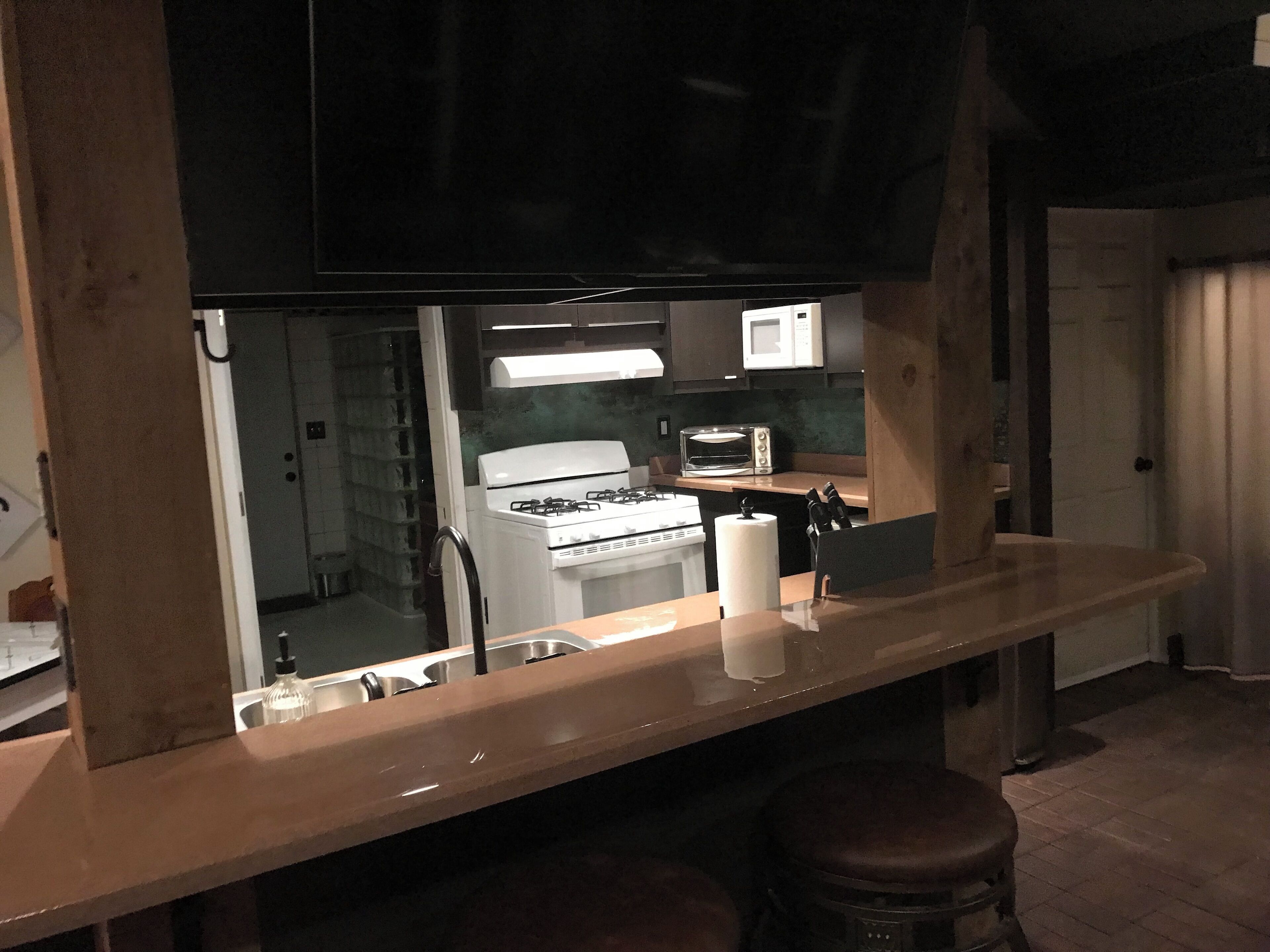 A kitchen with a stove, microwave, and toaster. There is a wooden counter and a stool.
