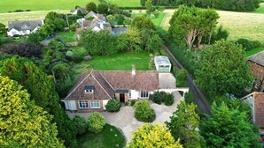 A large, single-story house with a sloped roof, surrounded by a well-maintained lawn and various trees. - Barton Lodge (Minehead)
