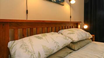 Una cama bien tendida con ropa de cama floral, un cabecero de madera y dos lámparas de lectura fijadas a la pared.