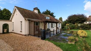 A single-story house with a sloped roof, a fenced driveway, and a garden with various plants and a small pond.