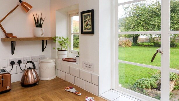 A kitchen with a wooden countertop, a kettle, a toaster, and a window with a view of a garden. - Barton Lodge (Minehead)