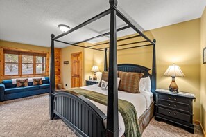Ein Bett mit Baldachin, ein blauer Sofa mit Kissen, ein Nachttisch mit Lampe und ein Fenster mit Jalousien.