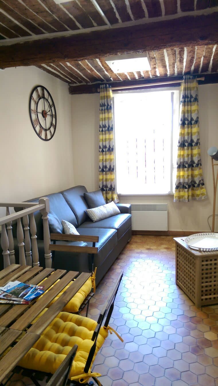 A living room with a blue sofa, wooden furniture, a hexagonal patterned floor, and a window with curtains.