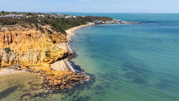 Paesaggio costiero con una scogliera rocciosa, acque turchesi cristalline e una spiaggia.