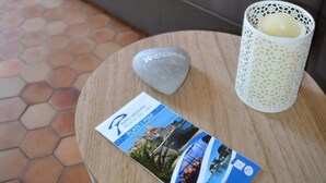 Un sofá gris con cojines estampados, una mesa redonda de madera con una piedra de bienvenida, una vela en un recipiente blanco y un folleto Plan Map.