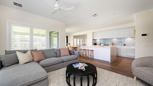 Una sala de estar moderna con un sofá seccional gris, una mesa de centro redonda, y una cocina con armarios blancos y un salpicadero azul.