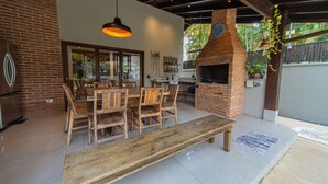 An outdoor patio with a brick oven, wooden furniture, and a hanging light fixture. - Casa com Piscina e rea Gourmet em Barra do Una (São Sebastião)