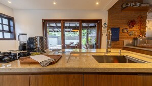 A modern kitchen with a granite countertop, wooden cabinets, and a large sink. - Casa com Piscina e rea Gourmet em Barra do Una (São Sebastião)