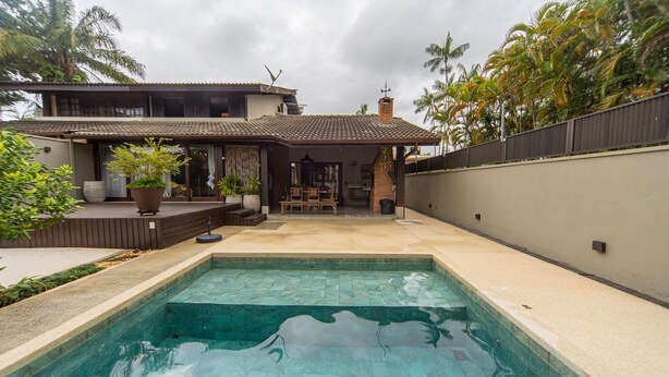 A swimming pool with a tiled deck, a covered patio area with seating, and a house with a tiled roof and a chimney. - Casa com Piscina e rea Gourmet em Barra do Una (São Sebastião)