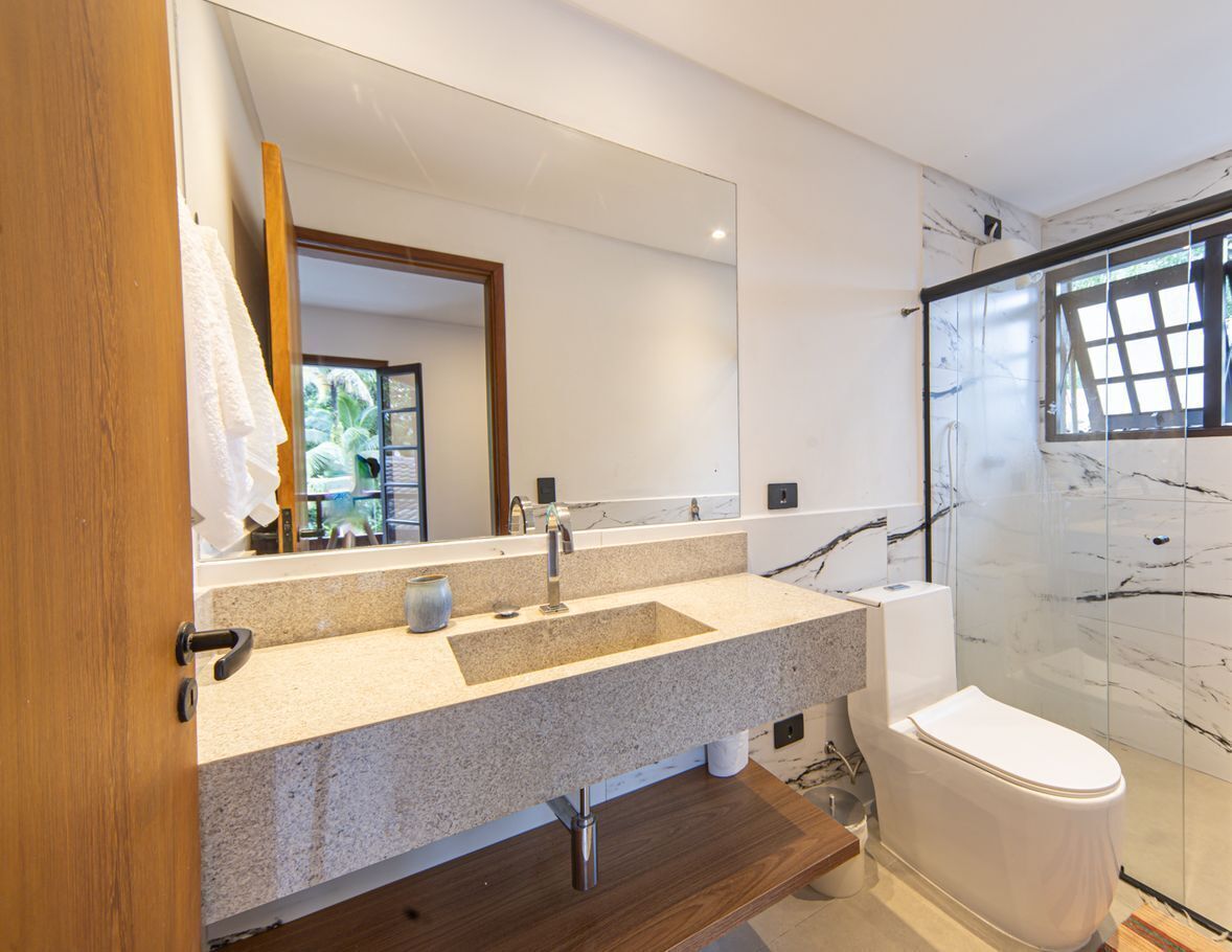 A modern bathroom with a granite countertop, a white toilet, and a glass shower enclosure.