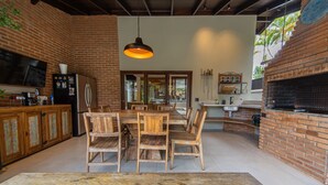 A rustic kitchen with a brick wall, wooden dining table, and chairs. - Casa com Piscina e rea Gourmet em Barra do Una (São Sebastião)