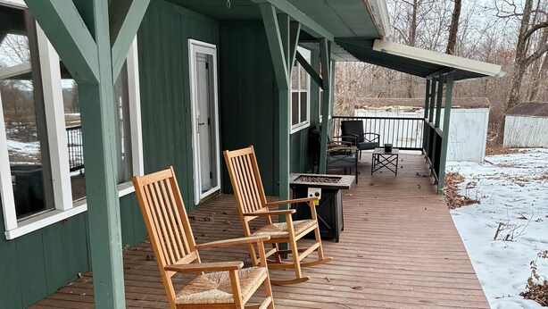 A covered wooden deck with rocking chairs and a grill area.