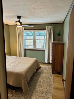 A bedroom with a bed, a ceiling fan, a window with curtains, a wooden cabinet, and a view of the outside. - Newly Renovated 3BR : Quartz Kitchen : Fast Fiber WiFi : Carport Parking (Campbell)