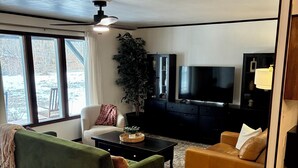 A living room with a green sofa, a brown leather sofa, a black entertainment unit, and a large window with a view of a snowy yard.