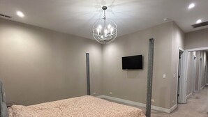 Ein Schlafzimmer mit Bett, einer Kandelaber, einem Flachbildfernseher und einem Flur mit Türen.