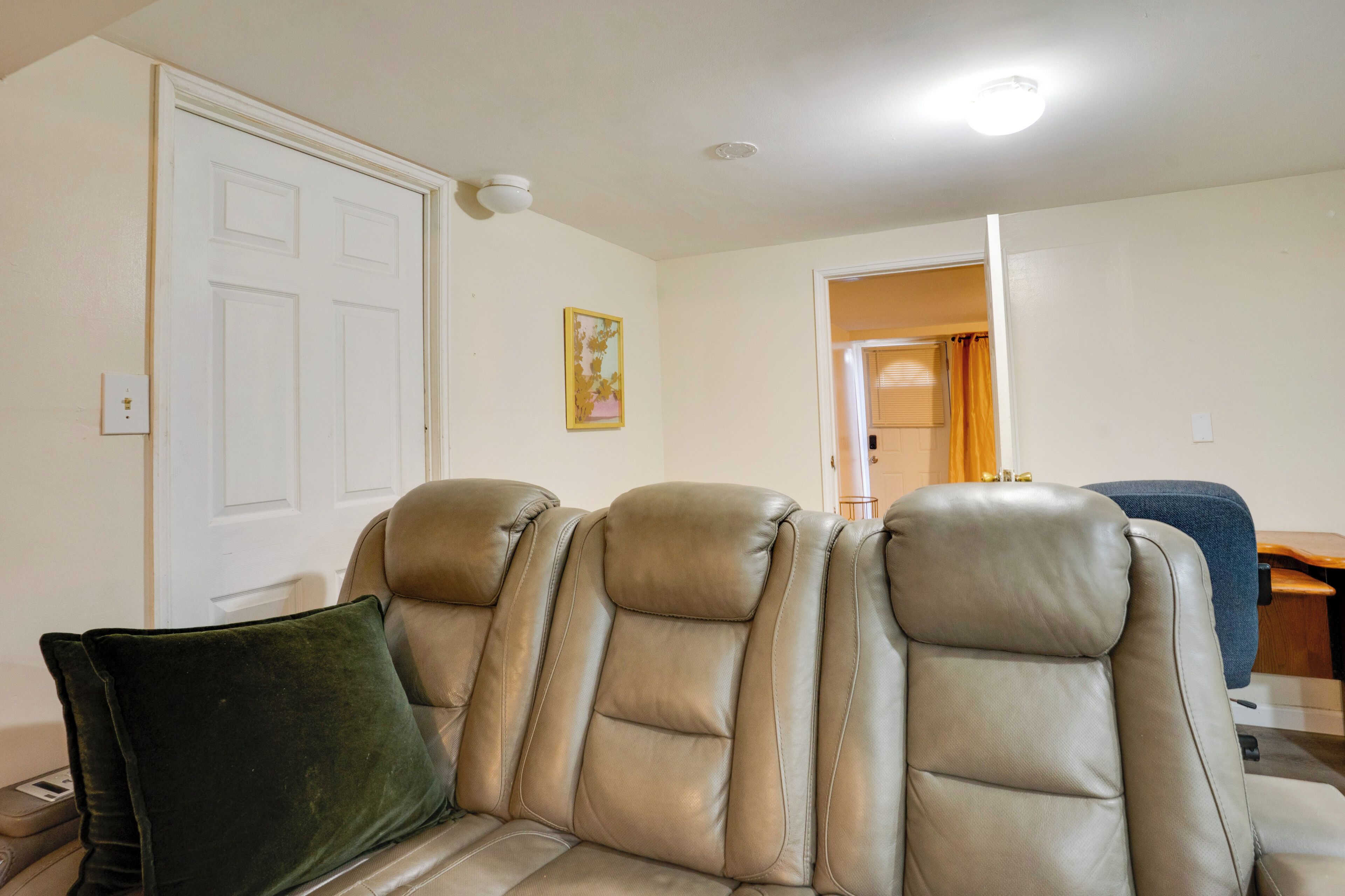 A beige leather sofa with a green pillow, a white door, and a framed picture on the wall.
