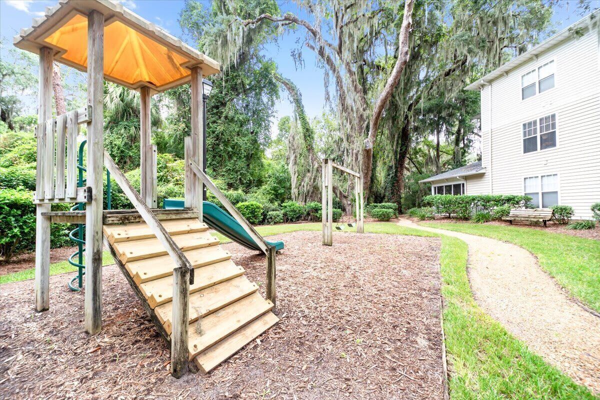 A wooden play structure with a slide, surrounded by mulch and trees.