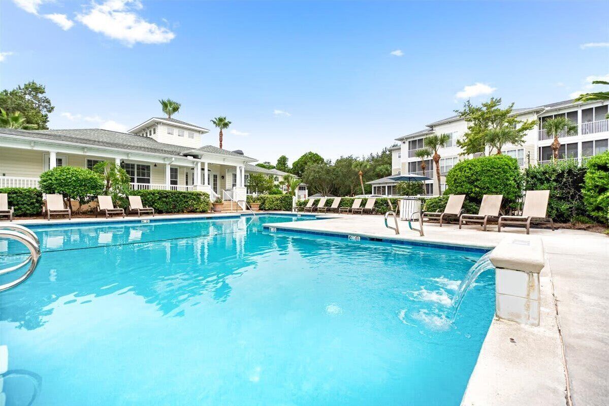 A swimming pool with lounge chairs, surrounded by buildings with balconies and palm trees.