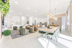 A spacious living area with a large dining table, modern furniture, and a staircase leading to an upper level. - Paradiso's Luxurious New Home w 15 Ensuites (Orlando)