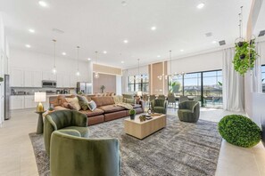 A modern living room with a sofa, armchairs, a coffee table, and a dining area with chairs. - Paradiso's Luxurious New Home w 15 Ensuites (Orlando)