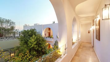 Un pasillo con paredes blancas, barandillas de vidrio y vistas a zonas verdes y edificios.