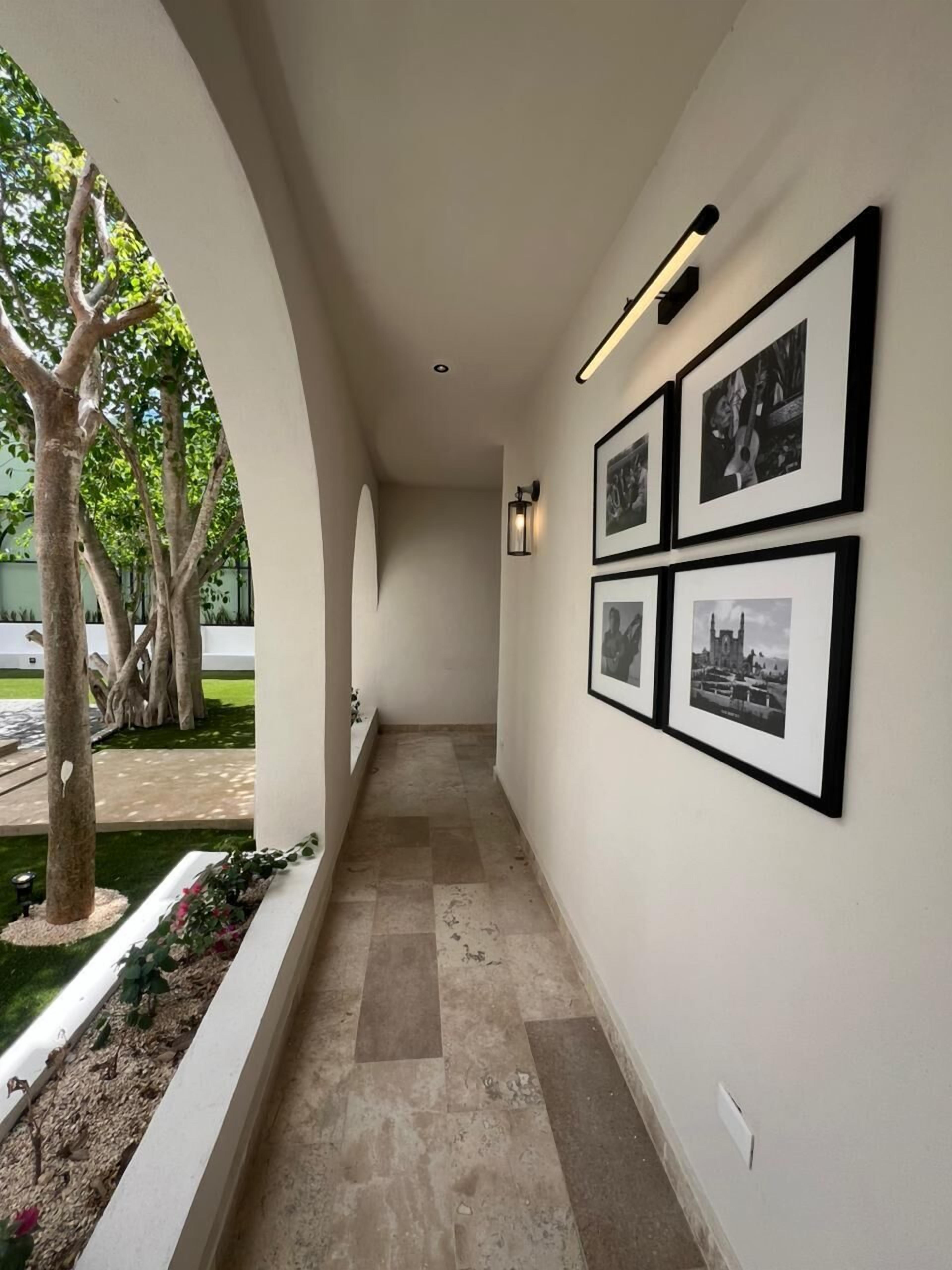 Un pasillo con cuadros en la pared, una lámpara y un árbol fuera.