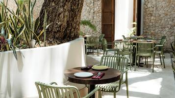 Un espace extérieur aménagé avec des tables et des chaises, un grand arbre et un mur en pierre.