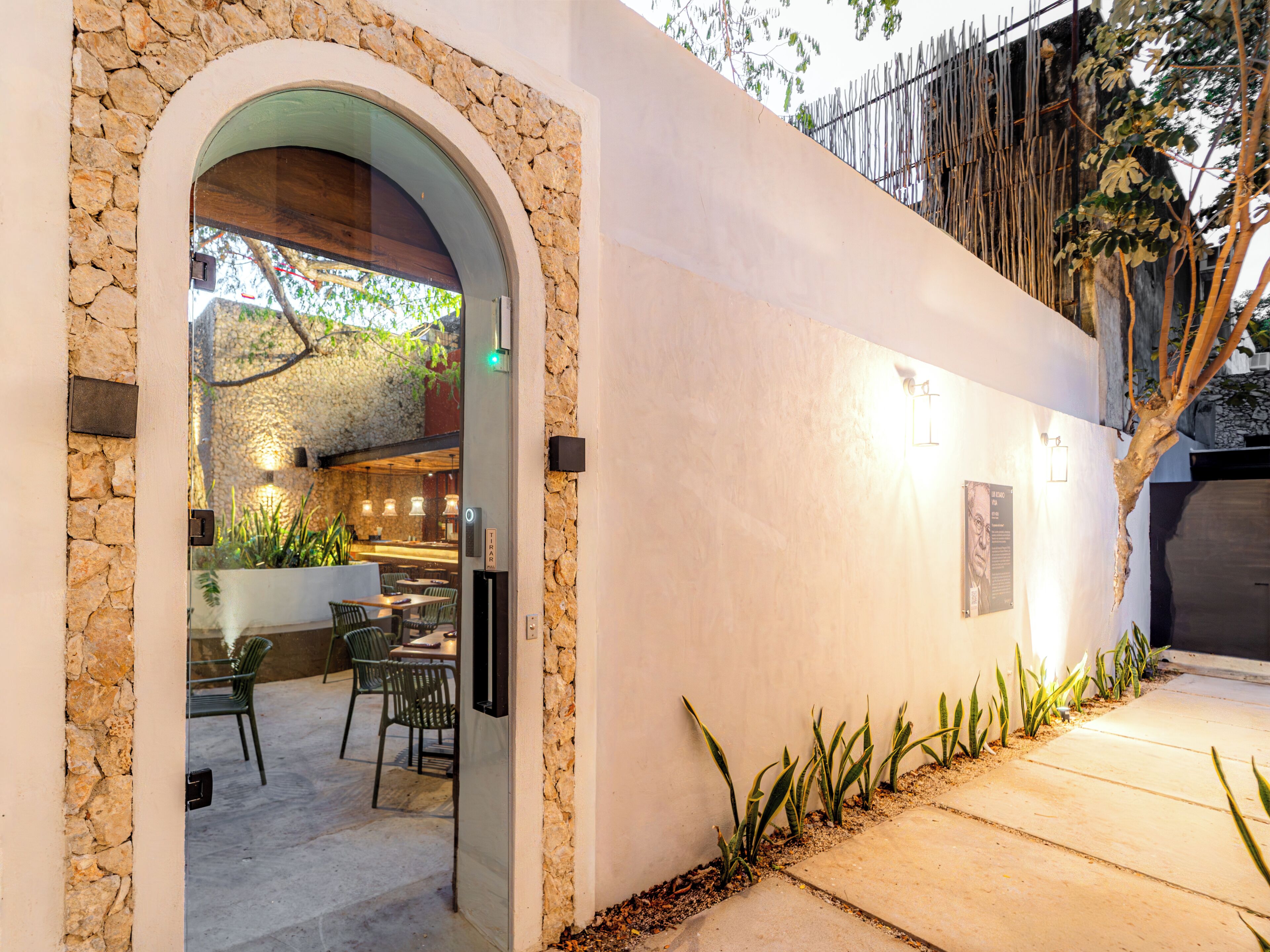 An outdoor dining area with stone walls, a wooden archway, and a seating arrangement.