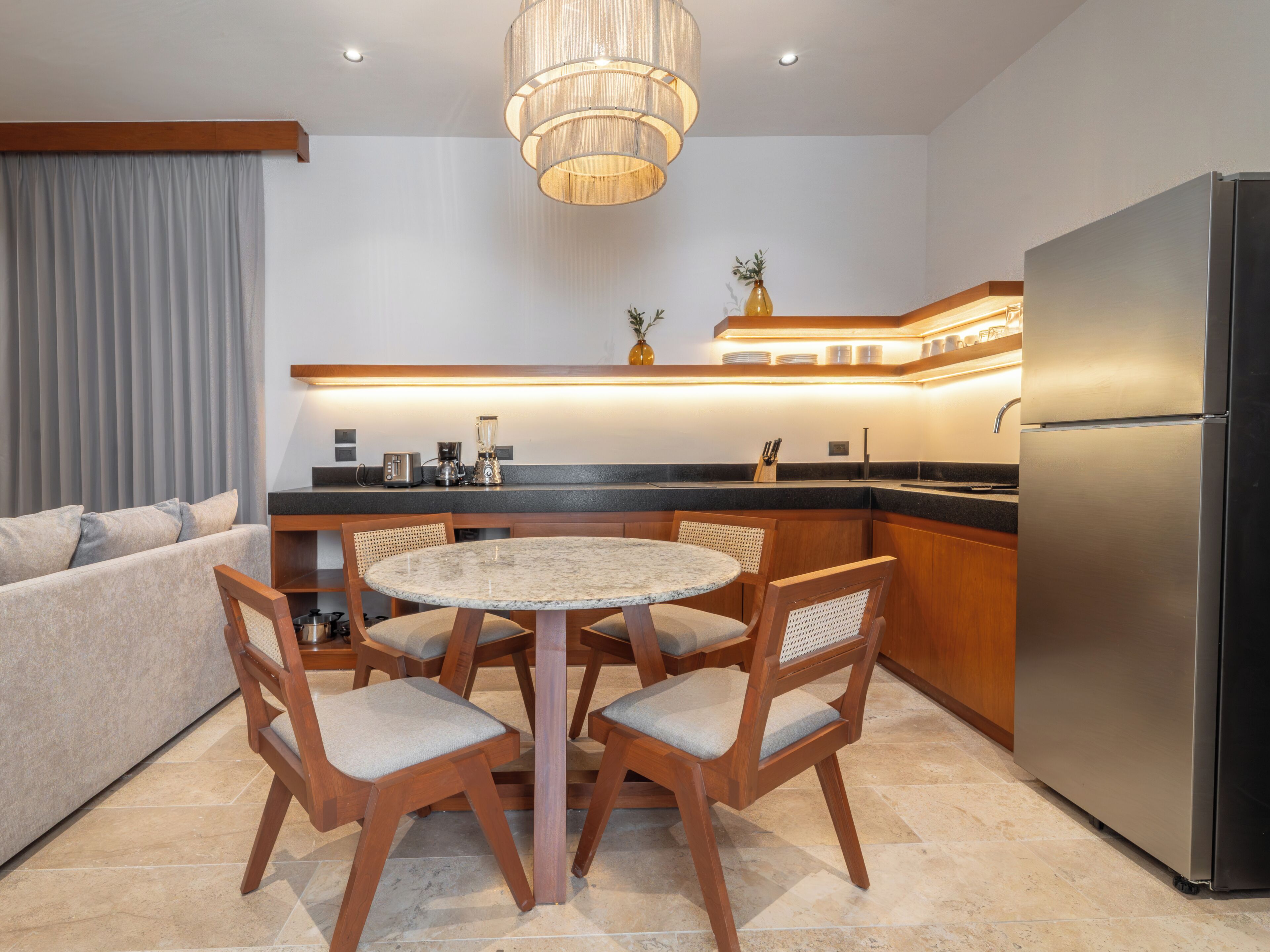 A modern kitchen with a dining area, including a round table and chairs, a refrigerator, and a built-in oven.