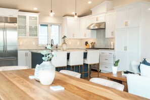 Una cocina moderna con armarios blancos, una mesa de comedor de madera y un refrigerador de acero inoxidable.
